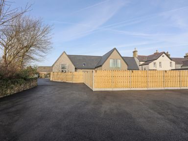 A paved driveway leading to a building with a wooden fence around the yard at Ysgol Fawr Big School in Benllech