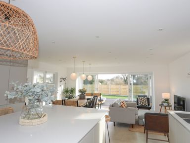 An open plan kitchen and living room with dining table chairs sofa and large sliding glass doors at Ysgol Fawr (Big School) in Benllech
