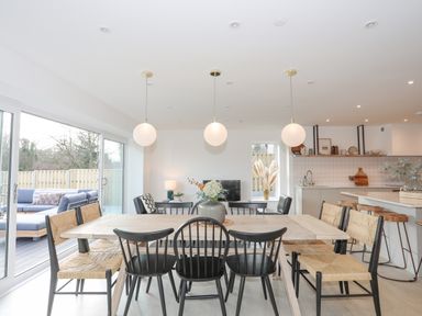 A dining area with a wooden table and mixed chairs near a kitchen with bar stools at Ysgol Fawr Big School in Benllech