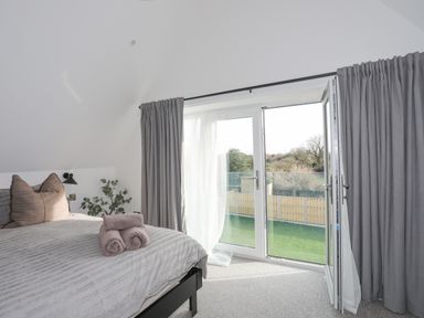 A bedroom with a bed pillows and towels near glass doors opening to a garden at Ysgol Fawr Big School in Benllech