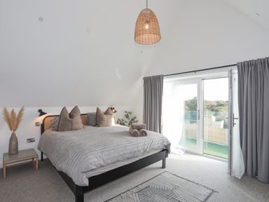 A bedroom with a bed a side table with a vase and French doors with curtains at Ysgol Fawr Big School in Benllech