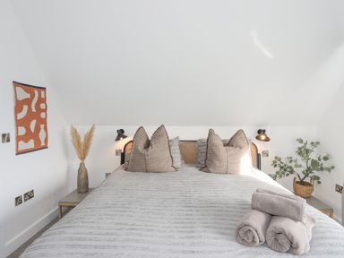 A bedroom with a bed with pillows and rolled towels bedside tables with plants and lamps at Ysgol Fawr Big School in Benllech