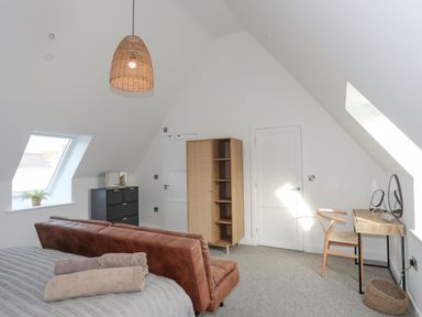 A bedroom with brown sofa a bed with towels on it a wicker lamp wooden shelves and a desk with a chair at Ysgol Fawr Big School in Benllech