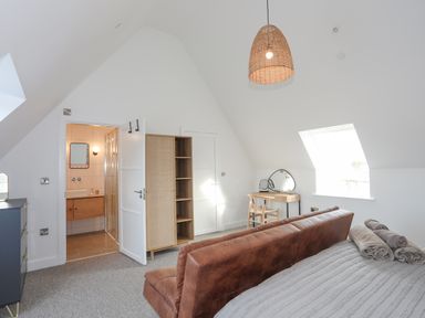 A bedroom with a bed folded towels a brown couch a wooden dressing table with mirrors an open door to a bathroom and a wooden wardrobe at Ysgol Fawr Big School in Benllech