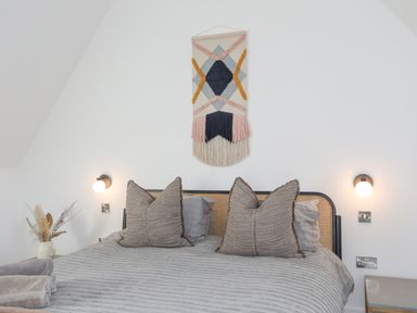 A bed with pillows and a textured blanket wall lamps and a decorative wall hanging above the bed at Ysgol Fawr Big School in Benllech