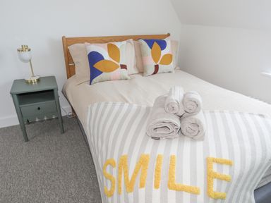 A bedroom with a wooden bed frame two patterned pillows folded towels on a striped blanket and a bedside table with a lamp at Ysgol Fawr Big School in Benllech