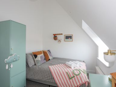 A bedroom with a bed with striped blanket and pillows next to a turquoise wardrobe and a window at Ysgol Fawr Big School in Benllech