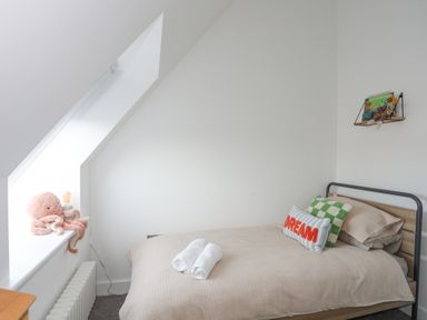 A bedroom with a single bed with pillows and towels near a window with a stuffed octopus toy and a small shelf with toys and books on the wall at Ysgol Fawr Big School in Benllech