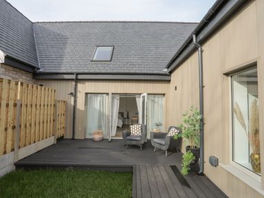 An outdoor patio area with two chairs a small table and plants outside a building with beige walls and a slanted roof with a skylight at Ysgol Fawr Big School in Benllech