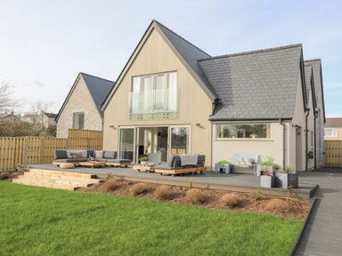 A modern house with a patio seating area and a lawn at Ysgol Fawr Big School in Benllech
