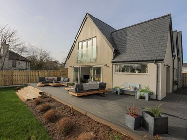 A backyard patio with outdoor seating and plants attached to a house with a fenced yard at Ysgol Fawr Big School in Benllech