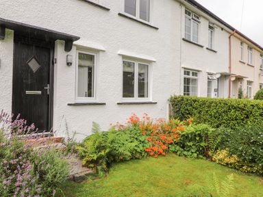 A row of white houses with black doors and windows and a garden with green grass flowers and bushes at 1 Millbank in Keswick