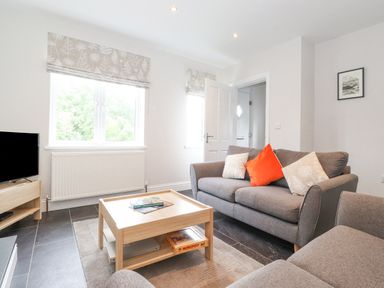 A living room with gray sofas and a wooden coffee table with books and a game at 1 Millbank in Keswick