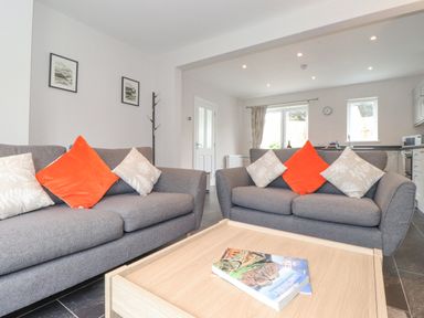 A living room with two grey sofas and orange and cream cushions at 1 Millbank in Keswick