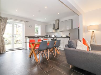 A kitchen and dining area with a glass table and mixed color chairs next to a gray sofa and a floor lamp at 1 Millbank in Keswick