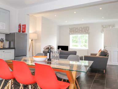 An open plan kitchen and living area with a glass dining table and red chairs at 1 Millbank in Keswick