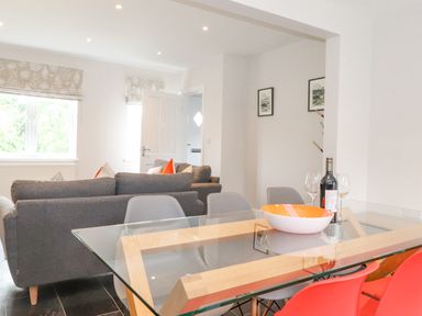 A dining area with a glass table and chairs next to a living room with gray sofas and orange cushions at 1 Millbank in Keswick