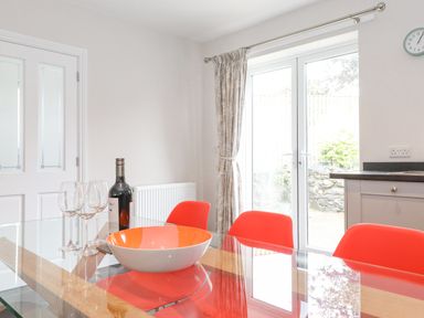 A dining area with a glass table with red chairs a wine bottle and glasses near double doors at 1 Millbank in Keswick