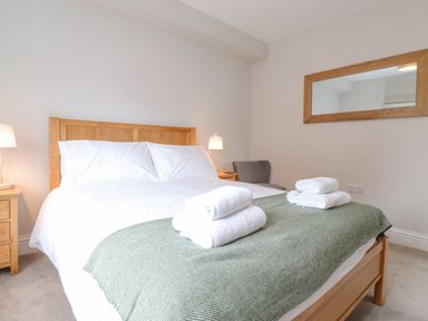 A bedroom with a wooden bed frame white bedding folded towels green throw blanket wooden nightstands lamps and a wall mirror at 1 Millbank in Keswick