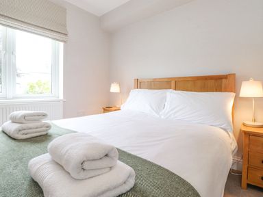 A bedroom with a wooden bed frame white bedding folded towels on a green blanket bedside tables with lamps at 1 Millbank in Keswick