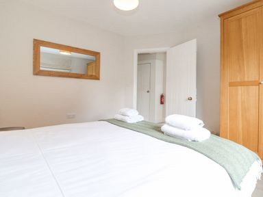 A bedroom with a bed covered with white sheets and green blanket with folded towels on top a wooden wardrobe a wall mirror and a partially open white door at 1 Millbank in Keswick