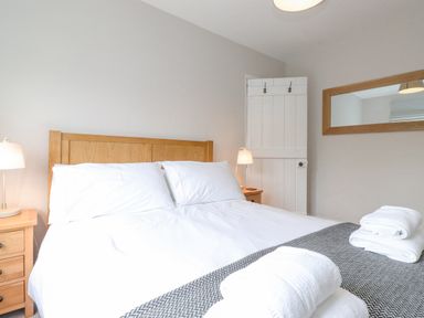 A bedroom with a wooden bed frame white bedding two bedside tables lamps and folded towels on the bed at 1 Millbank in Keswick