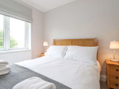 A bedroom with a wooden bed frame white bedding bedside tables with lamps and a window with a blind at 1 Millbank in Keswick