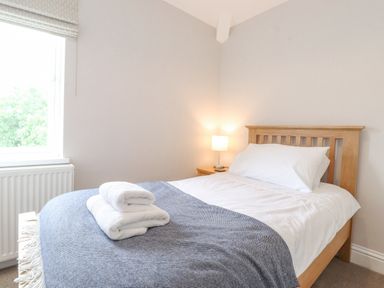 A bedroom with a wooden bed a bedside table with a lamp and towels on the bed at 1 Millbank in Keswick