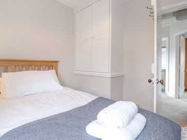 A bedroom with a bed with white linens a wooden headboard a gray blanket and folded white towels on top at 1 Millbank in Keswick
