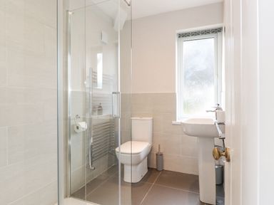 A bathroom with a shower, toilet, pedestal sink, and frosted window at 1 Millbank in Keswick