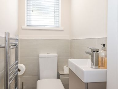 A small bathroom with a toilet a sink with a faucet and liquid soap and a window with blinds at 1 Millbank in Keswick