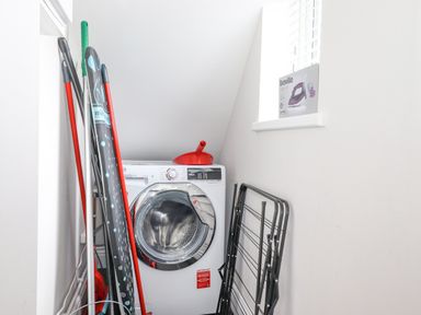 A laundry area with a washing machine an ironing board a drying rack and cleaning tools at 1 Millbank in Keswick
