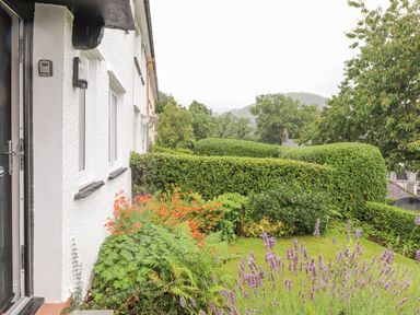 The exterior of a white house with a garden featuring hedges orange and purple flowers at 1 Millbank in Keswick