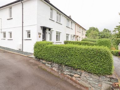 The exterior of a white two-story house with trimmed hedges and a stone wall along the sidewalk at 1 Millbank in Keswick