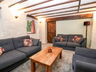 A living room with two sofas an armchair a wooden coffee table a floor lamp and wooden beams at Is Y Graig in Beddgelert