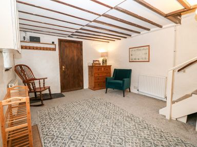 A small sitting area with a wooden rocking chair a green armchair a wooden chest of drawers and a patterned rug at Is Y Graig in Beddgelert
