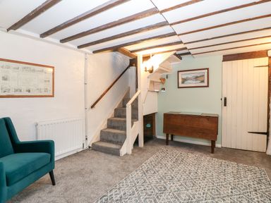 A living room with a staircase a green armchair a wooden table and framed pictures on the walls at Is Y Graig in Beddgelert