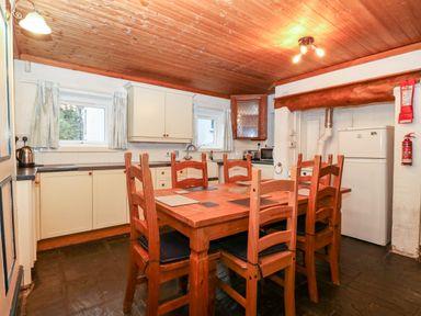 A kitchen with wooden dining table and chairs and white cabinets at Is Y Graig in Beddgelert