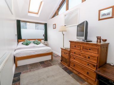 A bedroom with a wooden bed two green pillows a wooden dresser with a television and a floor lamp at Is Y Graig in Beddgelert