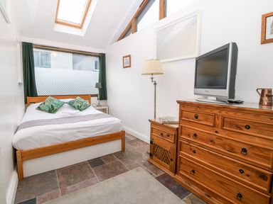 A bedroom with a bed green curtains wooden dresser and a television at Is Y Graig in Beddgelert