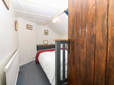 A small bedroom with a bed a dresser with a mirror pictures on the wall and a wooden door at Is Y Graig in Beddgelert