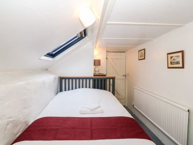 A small bedroom with a bed under a skylight and a wooden door at Is Y Graig in Beddgelert