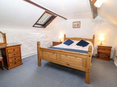 A bedroom with a wooden bed blue pillows a wooden dresser and two bedside tables with lamps at Is Y Graig in Beddgelert