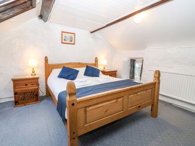 A bedroom with a wooden bed two bedside tables with lamps and two windows at Is Y Graig in Beddgelert
