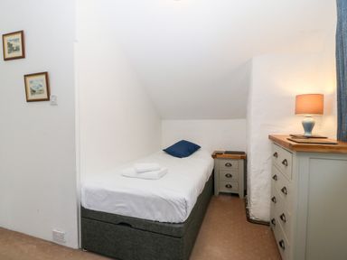 A small bedroom with a single bed a bedside table a chest of drawers and a lamp at Is Y Graig in Beddgelert