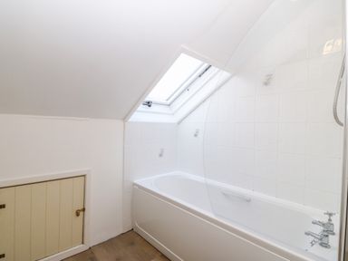 A bathroom with a bathtub under a slanted ceiling with a skylight window at Is Y Graig in Beddgelert