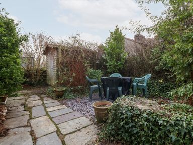 A garden with plastic chairs and a table near a wooden shed surrounded by bushes and plants at Is Y Graig in Beddgelert