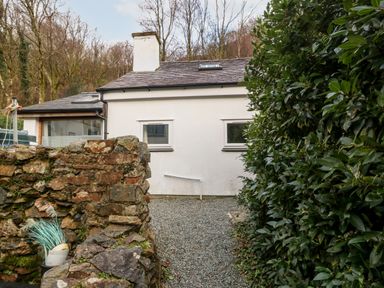 A white house with two small windows and a stone wall with plants at Is Y Graig in Beddgelert