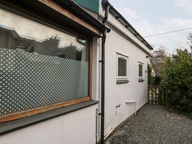 Exterior side view of a white building with three windows a gravel pathway and a wooden gate at Is Y Graig in Beddgelert