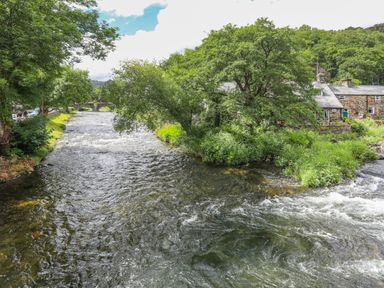 A river flowing through greenery with stone houses and a stone bridge in the background at Is Y Graig in Beddgelert
